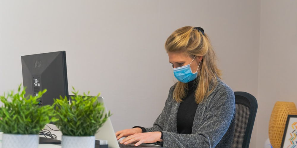 Woman working on the computer in an office whilst wearing a mask